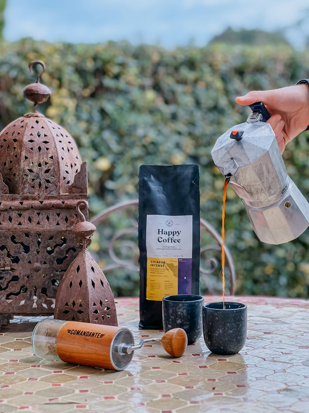 Hand pouring coffee from moka pot into a ceramic cup.